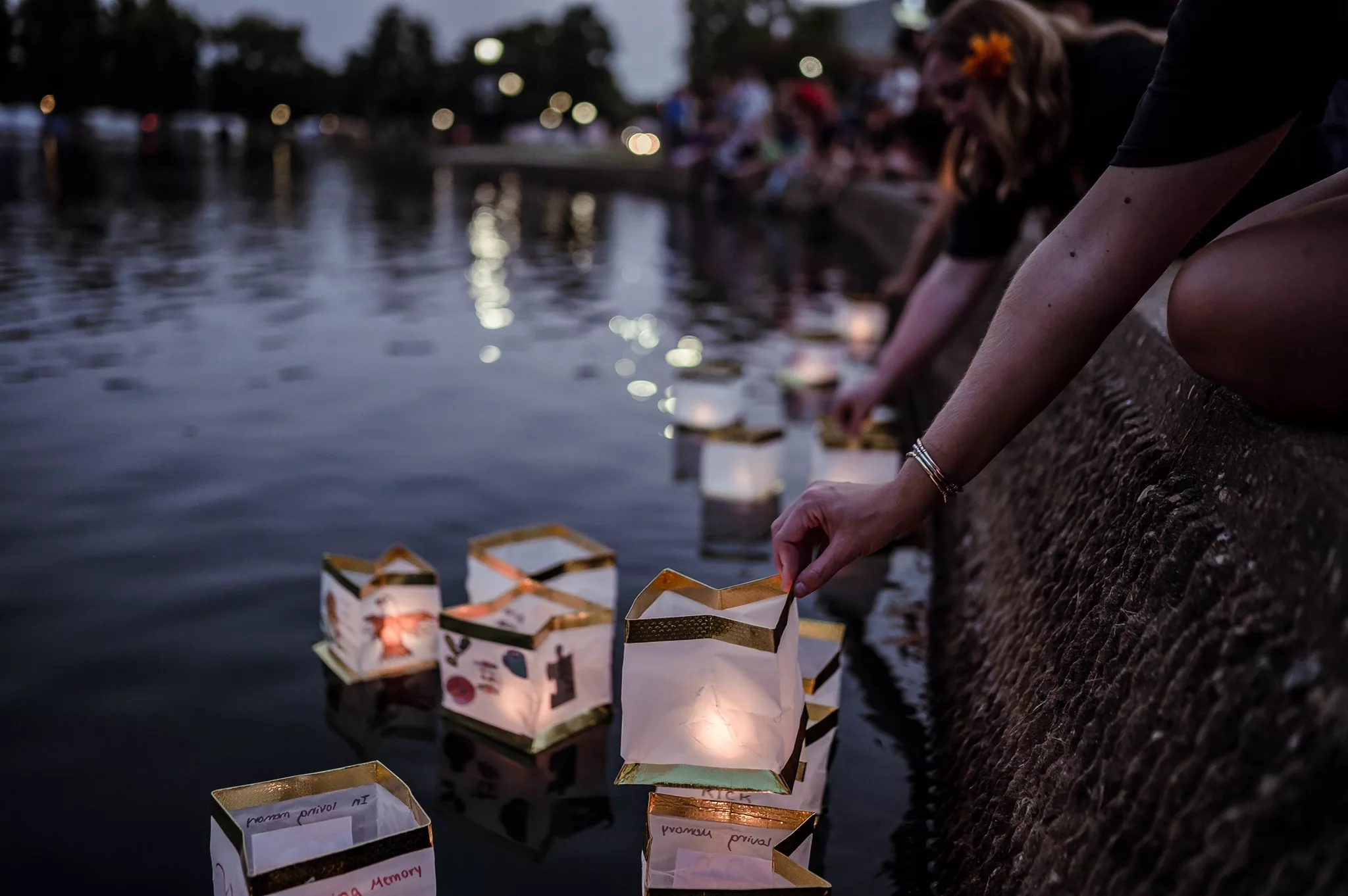 People placing floating lanterns onto a lagoon at night